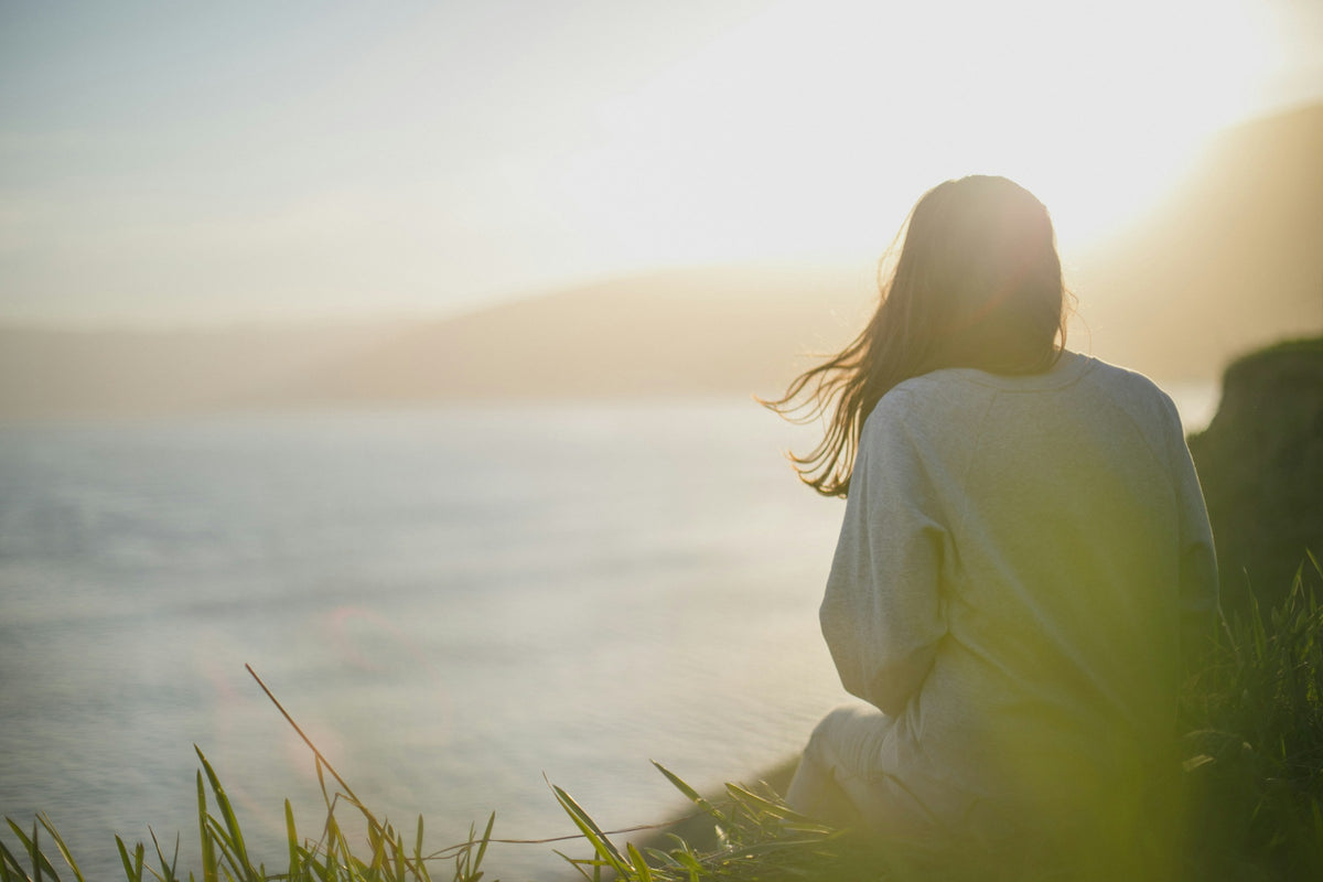 Femme assise face à la mer dans une lumière douce, qui respire calmement