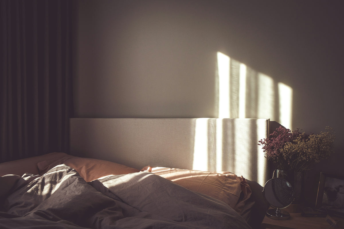 Chambre dans la pénombre où des rayons de lumière passent à travers les stores