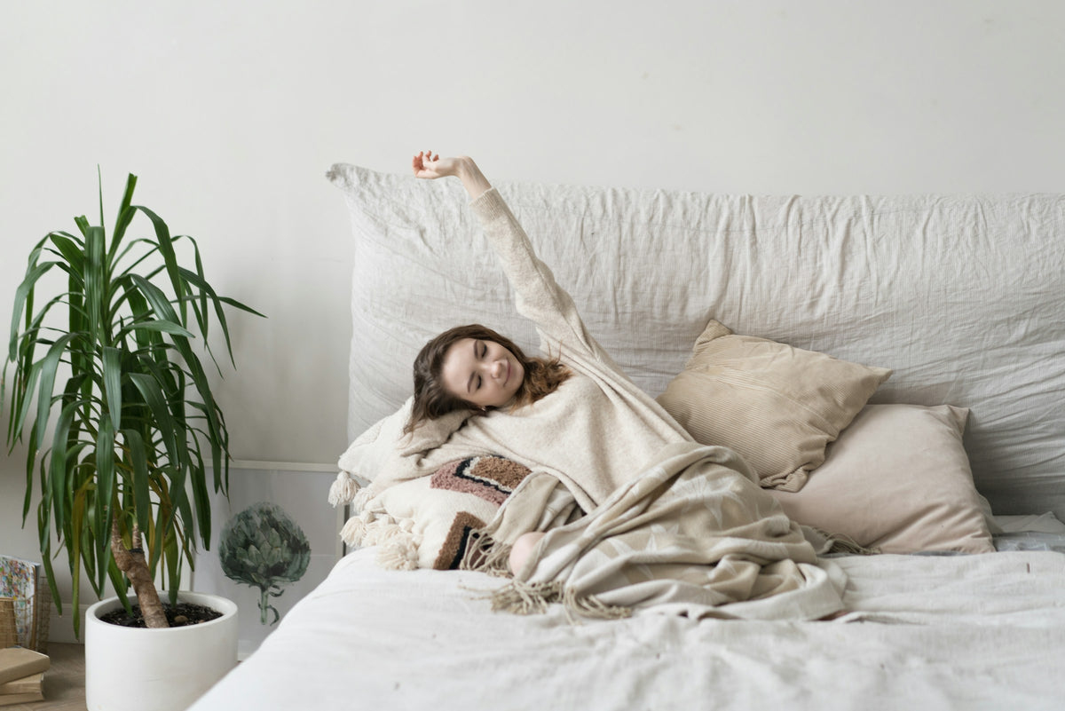 Femme qui s’étire tranquillement dans un lit aux draps clairs