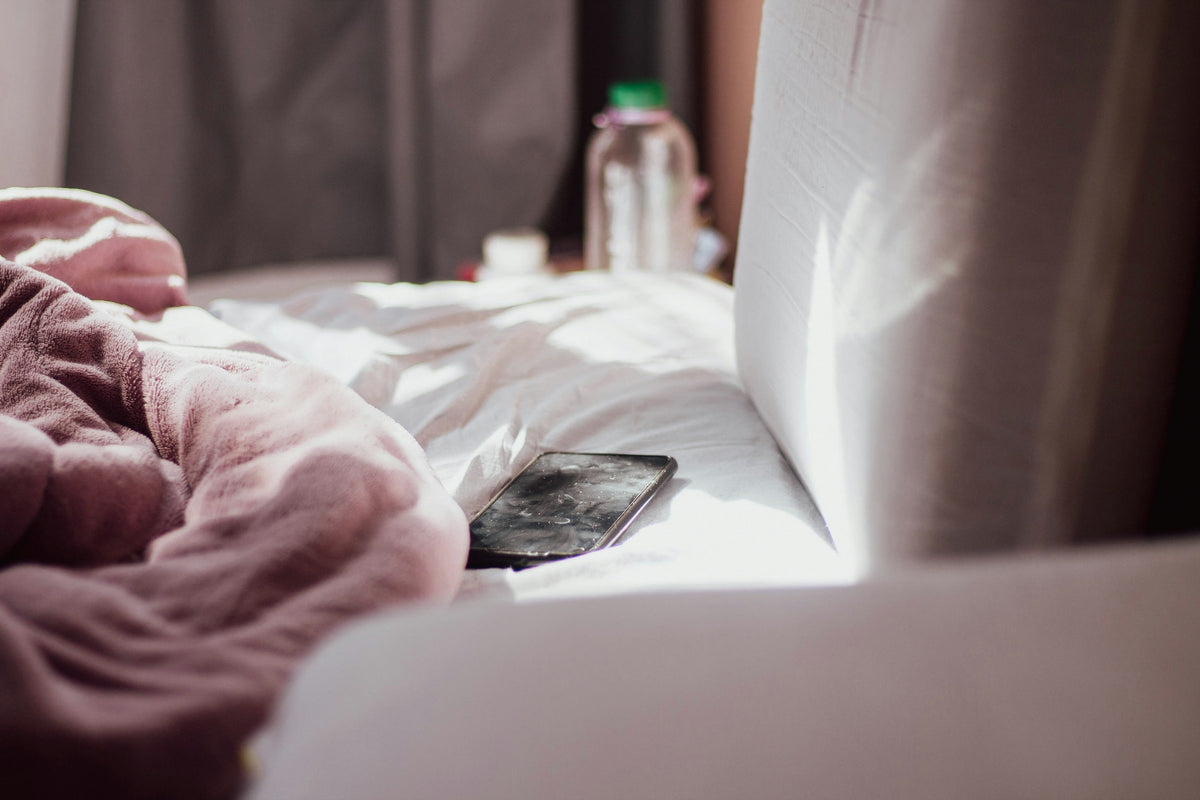 Téléphone posé sur un lit défait, dans une chambre baignée de lumière douce