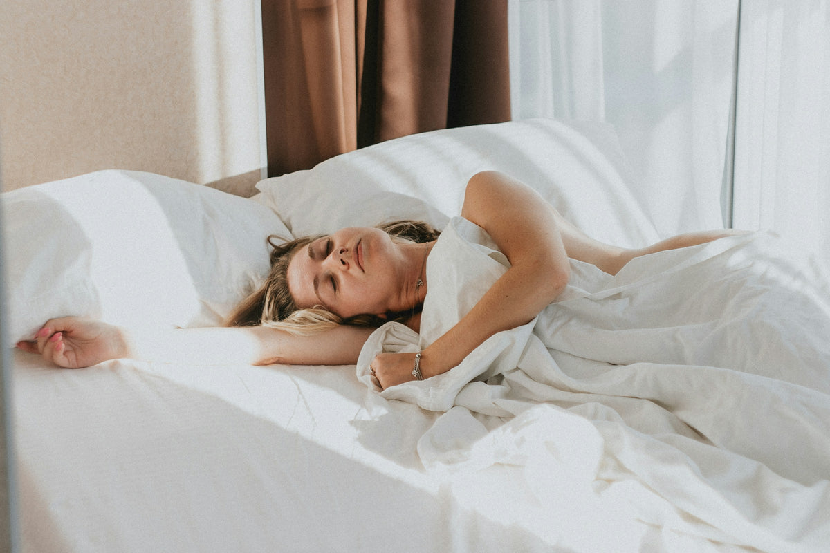 Femme qui s’endort paisiblement dans des draps blancs, à la lumière douce du matin