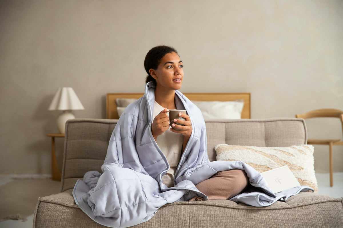 Femme enroulée dans un plaid, une tasse chaude à la main, qui se détend le soir