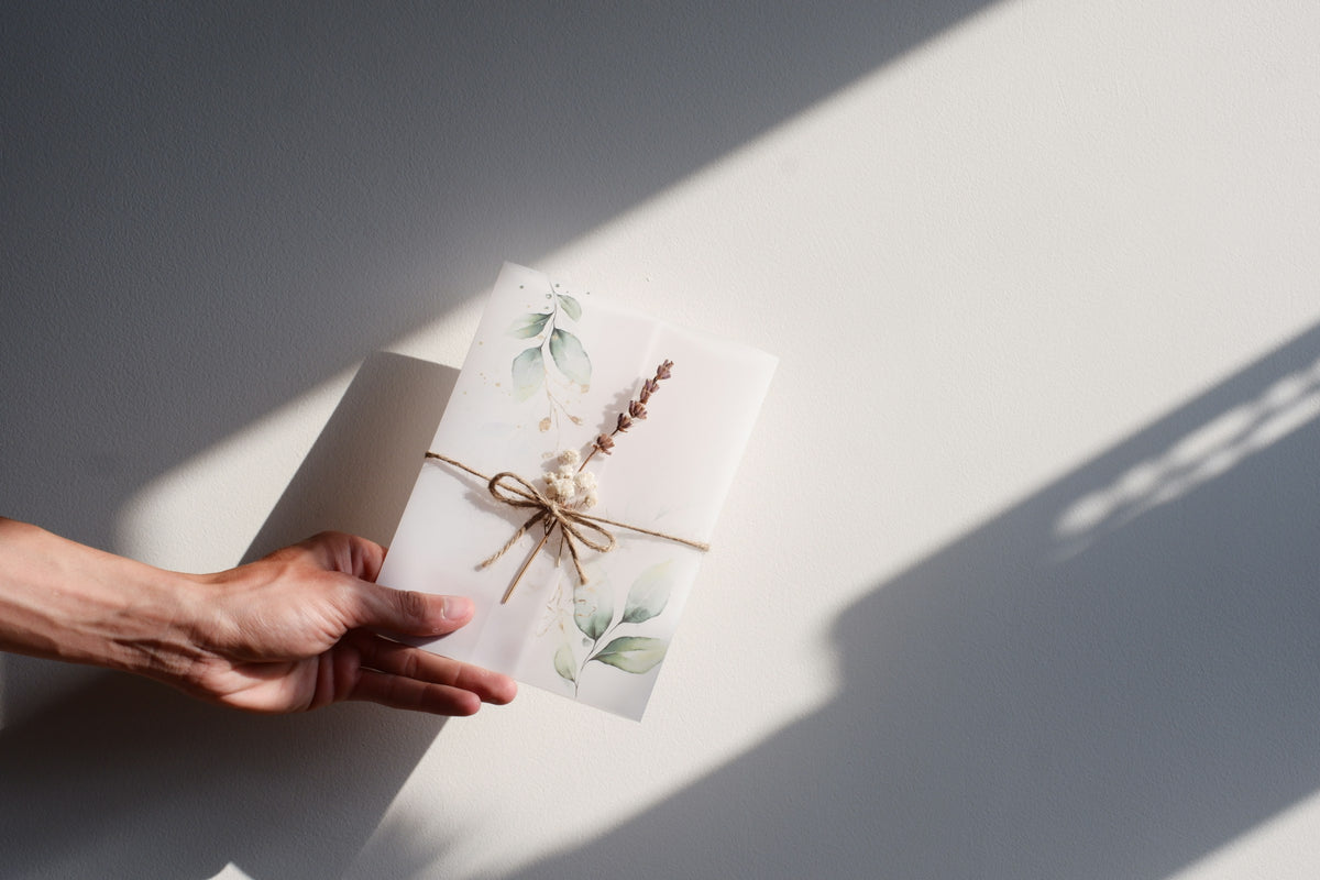 Main qui tend un petit cadeau emballé de papier blanc, de ficelle et d’un brin de lavande