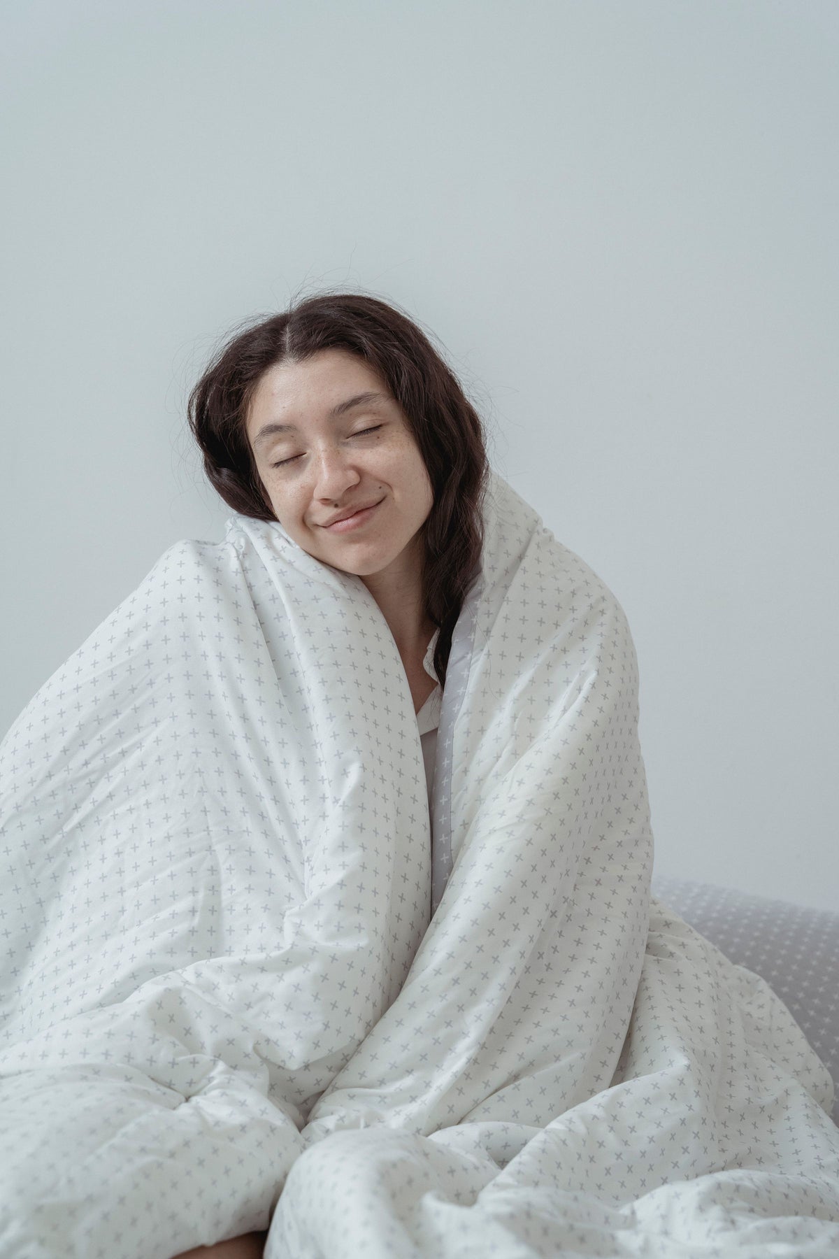 Femme souriante, les yeux fermés, emmitouflée dans une couette blanche