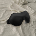 Masque de nuit Essentiel noir posé sur un drap froissé