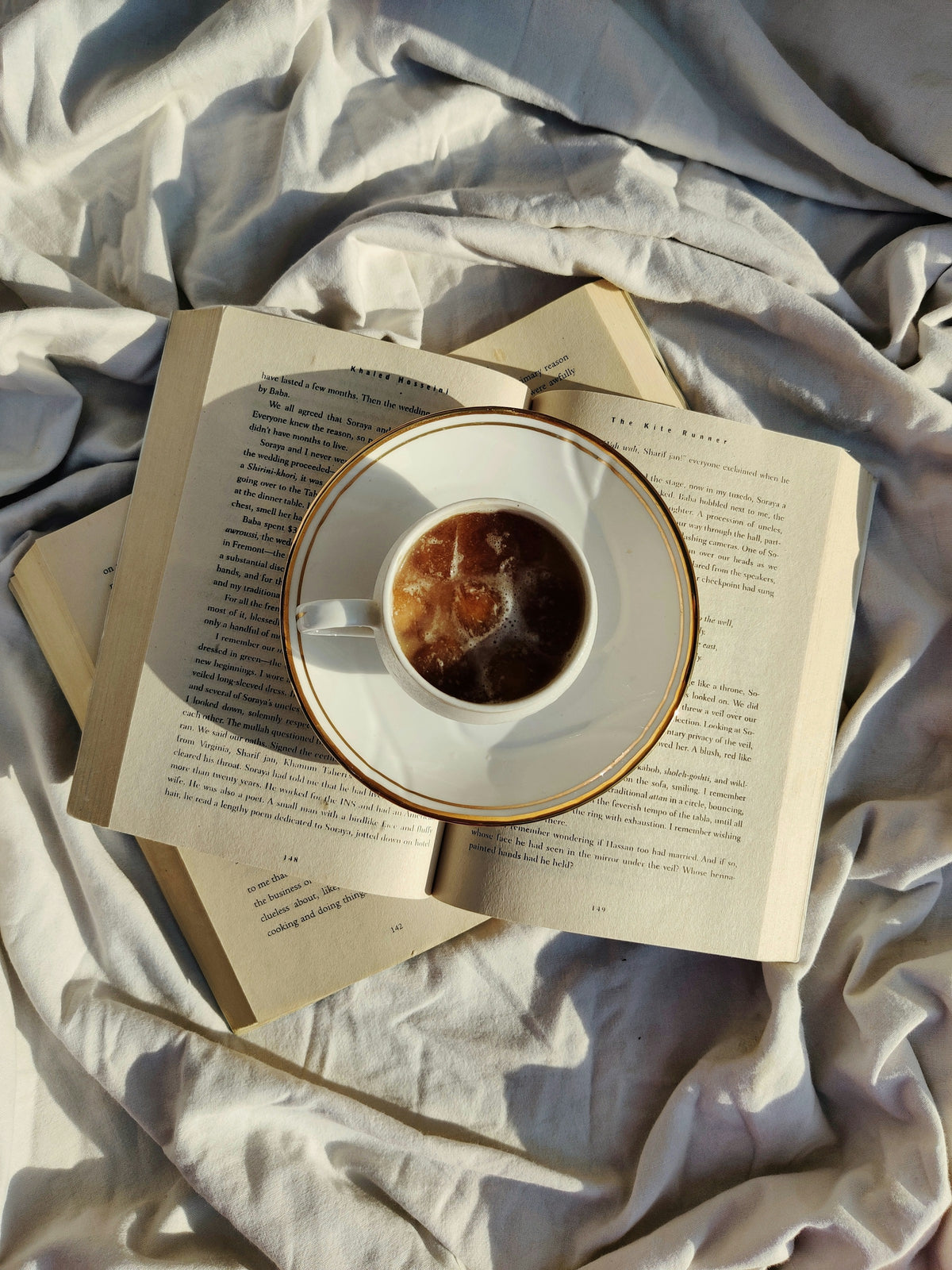 Un livre ouvert et une tasse chaude posés sur des draps froissés